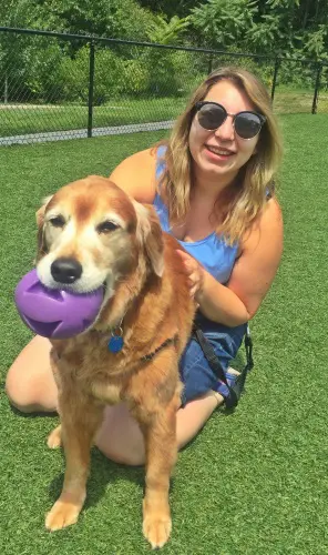 A woman holding a dog with a frisbee in her mouth.