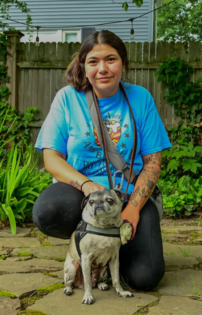 A woman kneeling down with her pug dog.