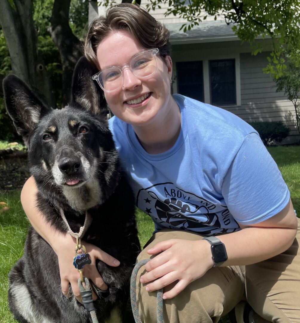 Person sitting with a black dog outdoors.